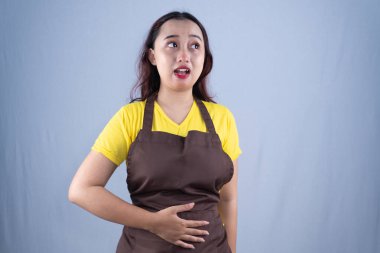 Sarı gömlekli ve kahverengi önlüklü bir kadın midesi bulanan bir ifadeyle yukarı bakıyor.