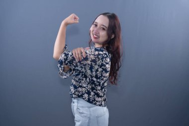 Lacivert çiçekli gömlekli ve kot pantolonlu bir kadın gülümsüyor ve sağ pazısını rahatça esnetiyor.