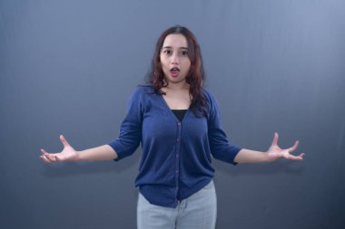 Mavi hırka giyen bir kadının ağzı ve elleri açıktır. Şok edici ya da şaşırtıcı olabilir.