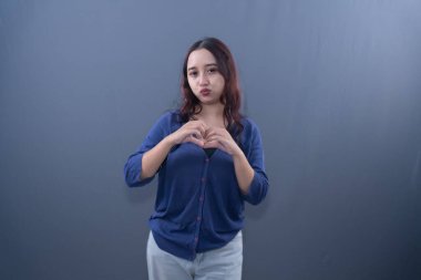 Mavi hırka giyen bir kadın elleriyle kalp şeklinde bir jest yapar ve yüzünü öper.