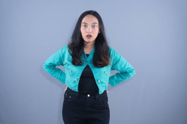 Deri ceketli ve siyah kotlu bir kadın elleri kalçasında, şaşırmış bir ifadeyle ayakta duruyor.