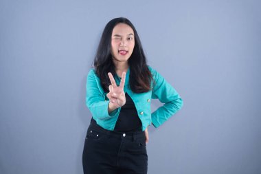 Deniz mavisi ceketli ve siyah kotlu bir kadın göz kırpıyor ve barış işareti yapıyor.