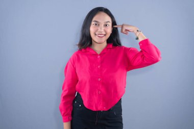 Pembe gömlekli bir kadın parmağıyla kameraya gülümsüyor.