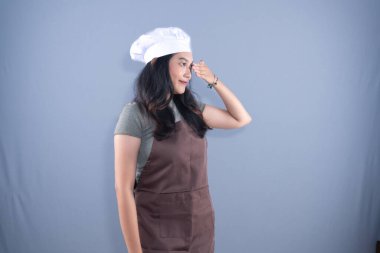 Şef şapkası ve kahverengi önlük takan bir kadın kollarıyla X işareti yapıyor.