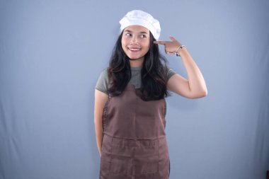 Şef şapkası ve kahverengi önlük takan bir kadın kollarıyla X işareti yapıyor.