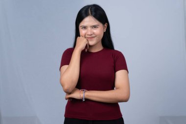 Kestane rengi tişörtlü gülümseyen genç bir kadın eli çenesinde poz veriyor.