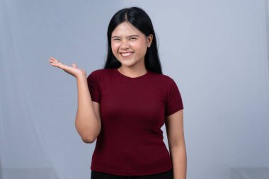 Kestane rengi tişörtlü genç bir kadın geniş bir gülümseme sergiliyor ve eli açık bir şey sunuyor.