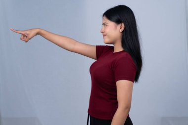 Kırmızı tişörtlü genç bir kadın kolunu uzatmış, arka planda gülümseyerek öne bakıyor.