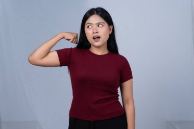 Kestane rengi tişörtlü genç bir kadın kaslarını esnetiyor ve ağzı açık bir şekilde yan tarafa bakıyor.