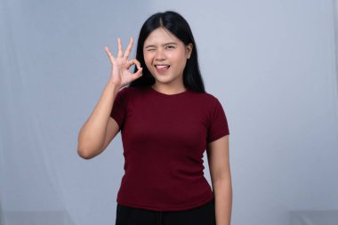 Bordo tişörtlü genç bir kadın göz kırpıyor ve el hareketi yapıyor.