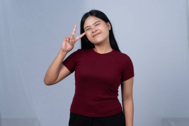 Bordo tişörtlü genç bir kadın barış işareti gösterirken göz kırpıyor.