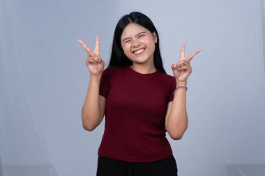 Bordo tişörtlü bir kadın heyecanla çifte barış işareti yapıyor.