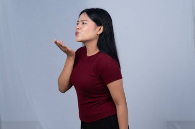 Kestane rengi tişörtlü genç bir kadın yan tarafa öpücük yolluyor.