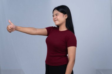 Kestane rengi tişörtlü kararlı bir kadın gergin bir gülümsemeyle baş parmağını kaldırır.