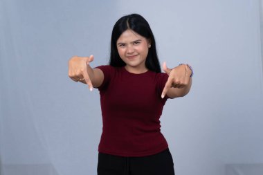 Kestane renkli tişörtlü bir kadın gülümseyip iki eliyle aşağıya işaret ediyor.