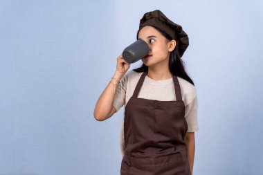 Kahverengi önlüklü ve şapkalı bir kadın şef bardaktan su içiyor.