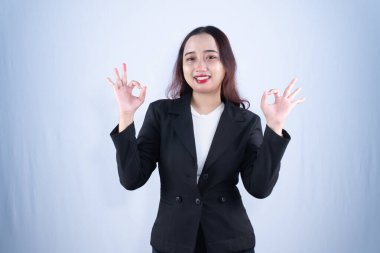 Siyah ceketli ve beyaz bluzlu neşeli bir Asyalı iş kadını iki eliyle onay işareti veriyor.