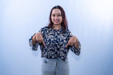 Çiçekli bluz giyen mutlu bir Asyalı kadın her iki işaret parmağıyla beyaz arka planı işaret ediyor.