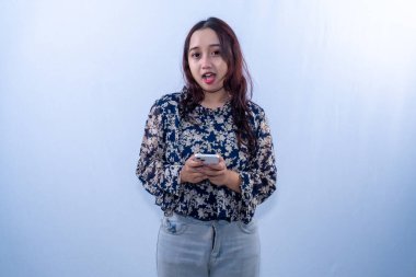 Çiçekli bluz giyen Asyalı bir kadın, ağzı açık akıllı bir telefonu tutarken şok olmuş gibi görünüyor.