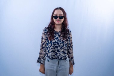 Çiçekli bluz ve güneş gözlüklü mutlu bir Asyalı kadın beyaz arka planda kameraya gülümsüyor.