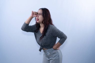 Gri tişörtlü Asyalı bir kadın elini gözlerinin üstüne koyup yan tarafa bakarken dilini uzatıyor.