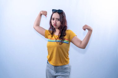 Sarı tişörtlü Asyalı bir kadın somurtkan veya somurtkan bir ifadeyle pazılarını esnetiyor.