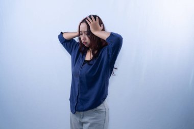 Mavi hırkalı, sıkıntılı genç bir kadın beyaz bir arka plana karşı acısını ya da hayal kırıklığını ifade ederek başını tutuyor.