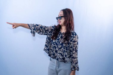 Mavi çiçekli bluzlu, gri pantolonlu ve güneş gözlüklü bir kadın solu işaret ediyor.