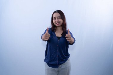 Mavi hırkalı, gülümseyen genç bir kadın beyaz bir arka plana karşı iki kez onay veriyor.