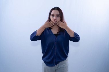 Mavi hırka ve açık gri pantolon giyen genç bir kadın ağzını şaşkınlıkla kapatıyor.