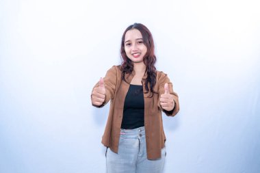 Kahverengi saçlı, gülümseyen bir kadın iki parmağını kaldırır. Kahverengi gömlek ve gri pantolon giyiyor.