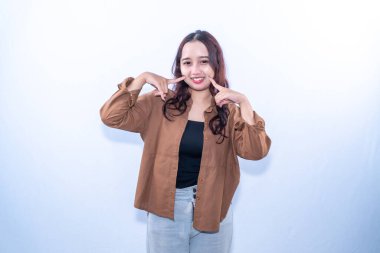 Kahverengi gömlekli, koyu kırmızı saçlı ve gri pantolonlu gülümseyen bir kadın yanaklarını işaret ediyor.