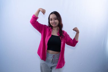 Pembe gömlekli, gri pantolonlu, koyu renk saçlı gülümseyen bir kadın kaslarını esnetiyor.