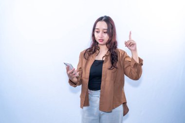 Kahverengi gömlekli genç bir kadın telefonuna bakarken bir fikri işaret ediyor.