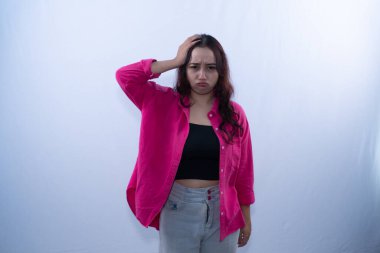 Pembe gömlekli genç bir kadın, beyaz bir arka planda hayal kırıklığına uğramış bir şekilde başını tutuyor.