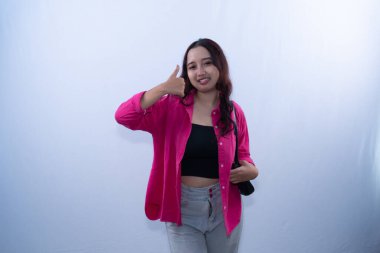 Pembe tişörtlü ve gri pantolonlu gülümseyen bir kadın beyaz bir arka plana başparmak sallıyor.