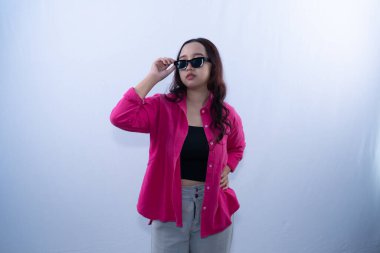 Pembe gömlekli ve gri pantolonlu kendine güvenen genç bir kadın güneş gözlüğünü ayarlar ve poz verir.