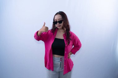 Güneş gözlüklü genç bir kadın, pembe gömlek, siyah bluz ve gri pantolon giyiyor.