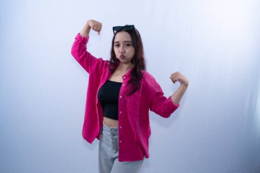 Pembe gömlekli ve güneş gözlüklü genç bir kadın kaslarını esnetiyor, kendinden emin görünüyor.