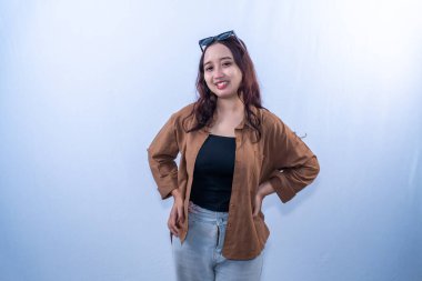 Kahverengi gömlekli ve açık renk pantolonlu gülümseyen genç bir kadın elleri kalçasında poz verir.