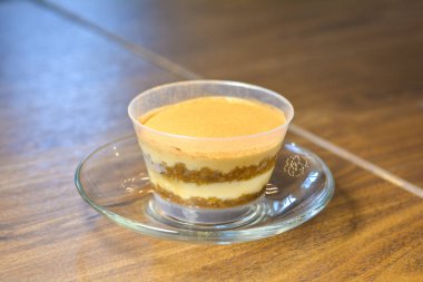 Bir kahve dükkanında, sıcak bir ışıkta, ahşap bir masanın üzerindeki bir fincan tiramisuyu kapat..