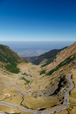 Transfagarasan otoyolunun keskin kıvrımları güneş ışığıyla aydınlanan dağ manzarasında zikzak çiziyor. Fagaras dağları, Romanya. Seyahat kavramı.