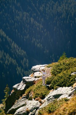 Romanya 'nın Fagaras Dağları' ndaki derin orman vadisinde uçurumun kenarında genç bir kadın. Transfagarasan otoyolu. Özgürlük, yalnız seyahat, farkındalık konsepti.