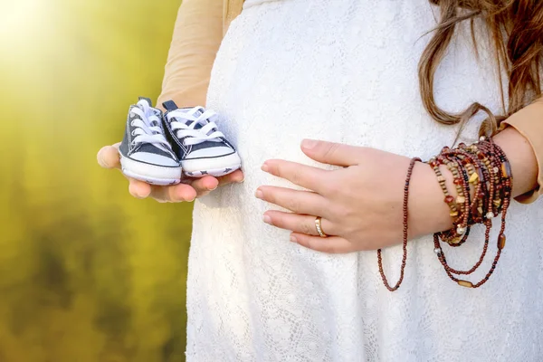 Zwanger vrouw buik houden baby laarzen. — Stockfoto