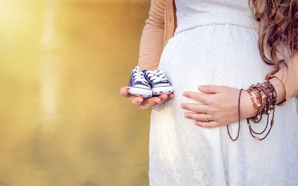 Schwangeren Bauch hält Baby Booties. — Stockfoto