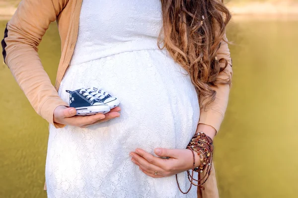 Zwanger vrouw buik houden baby laarzen. — Stockfoto