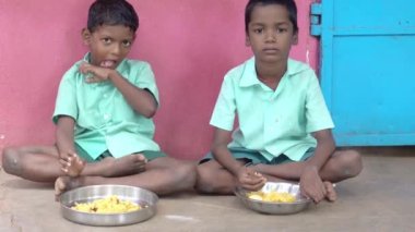 Teşhis edilemeyen, üniformalı, dışarıda oturan, sağ eliyle biraz pirinç yiyen zavallı sınıf arkadaşları. Devlet okulunda öğle yemeği, sağlıksız yemekler.