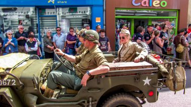 Aziz Michael L 'Eglise, FRANSA - 6 Haziran 2019. Normandiya Çıkarması 'nın kutlanması, silahlı çıkarma, İkinci Dünya Savaşı' nın Normandiya 'da sona ermesi, müttefik ülkelerin yardımıyla. Askerler sokakta izleyicilerle birlikte cipte yürüyorlar.