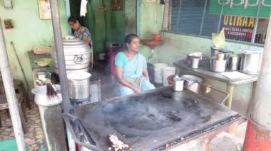 PUDUCHERRY, İNDİA - Aralık 2019. Sokak restoranında oturan bir kadın, pişmeye hazır, müşterileri bekleyen bir chapati. Müşteri yoksa iş de yok.