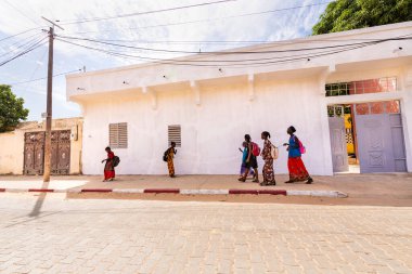 Bour, Senegal - 2021 Temyiz Dairesi. Kimliği belirsiz, okul çağındaki, sırt çantalı kızlar, güneşli bir bahar günü okuldan sonra fakir köyde yürüyorlar. Covid 19 pandemisi sırasında yüz maskesi yok..